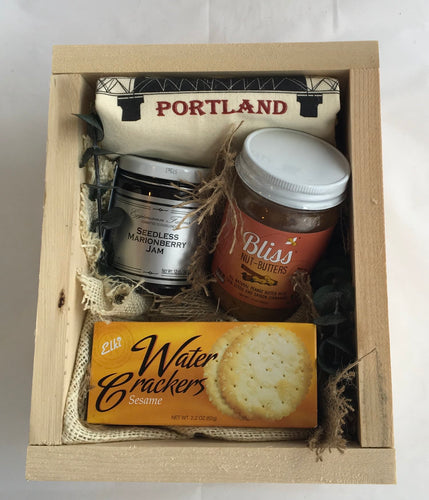 Sample box containing crackers, nut butter, jam, and a tea towel. 